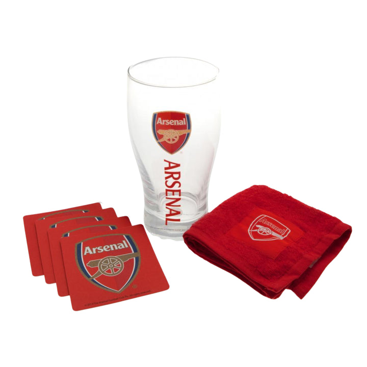 Arsenal glassware set including a clear pint glass with red Arsenal branding, four red coasters, and a folded red towel, all arranged on a white background.