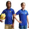Two children modeling matching blue Nike Chelsea soccer polo shirts against a white background, with one holding a yellow soccer ball.
