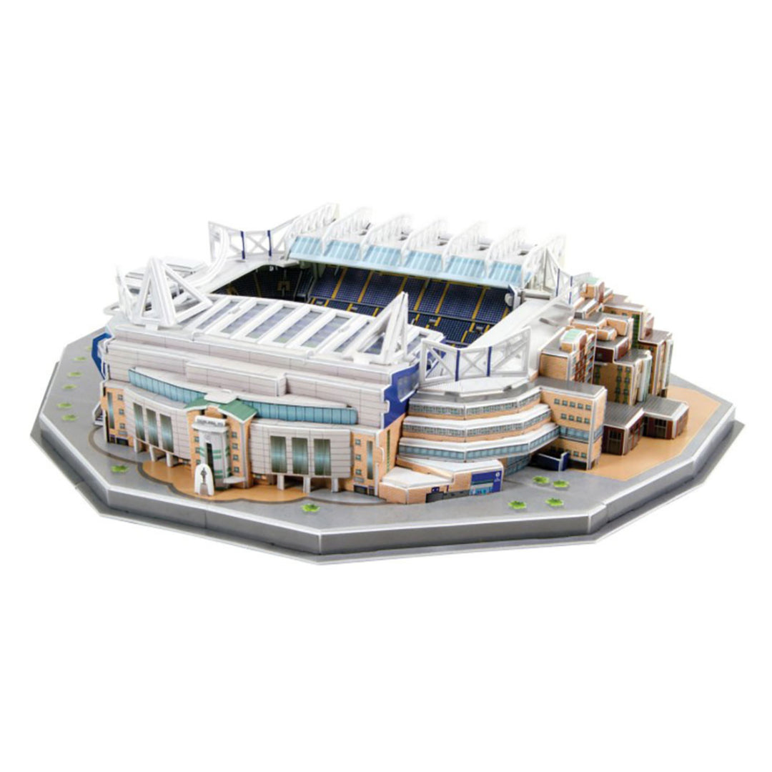 A detailed 3D model kit of a football stadium, shown from an elevated perspective on a clean white background. The model features white and blue stands, a dark blue central field, and surrounding stadium infrastructure in beige, brown, and gray tones.