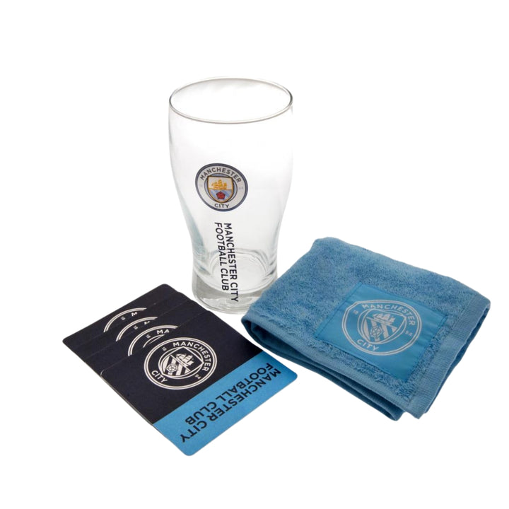 Manchester City branded glass, towel, and coasters on a white background