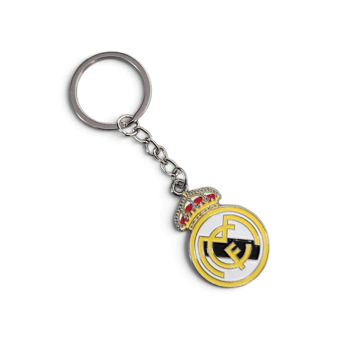 A silver metal keychain featuring a Real Madrid crest charm with a gold and white circular design, black details, and a small red and gold crown on a white background.