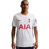 A man modeling a white Nike Tottenham Hotspur football jersey with red AIA sponsor text, a navy swoosh, and a navy club crest, set against a plain light gray background.
