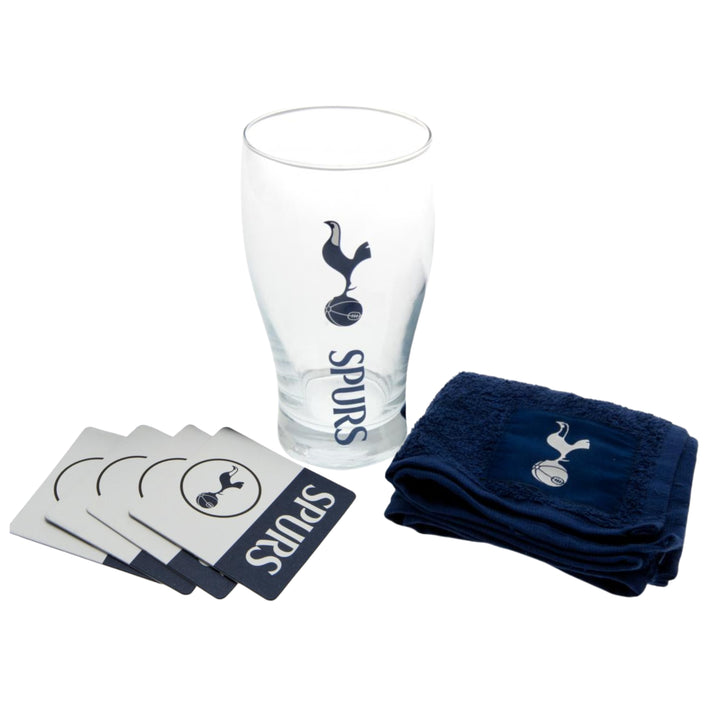 A Tottenham Hotspur-themed drinking set on a white background, including a clear glass with a navy logo, four silver coasters with navy ends, and a navy towel with a silver logo.